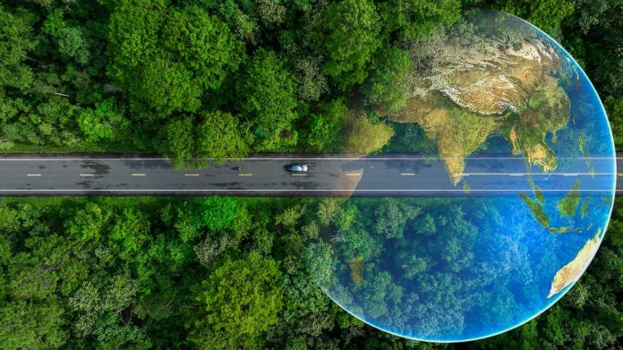 Vista aérea de um carro dirigindo em uma estrada rodeada de uma floresta. A imagem é composta por um globo simbolizando ecoenergia e sustentabilidade.