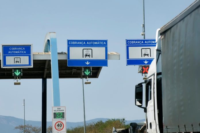 Caminhão passando por uma praça de pedágio automático em uma rodovia do Brasil.