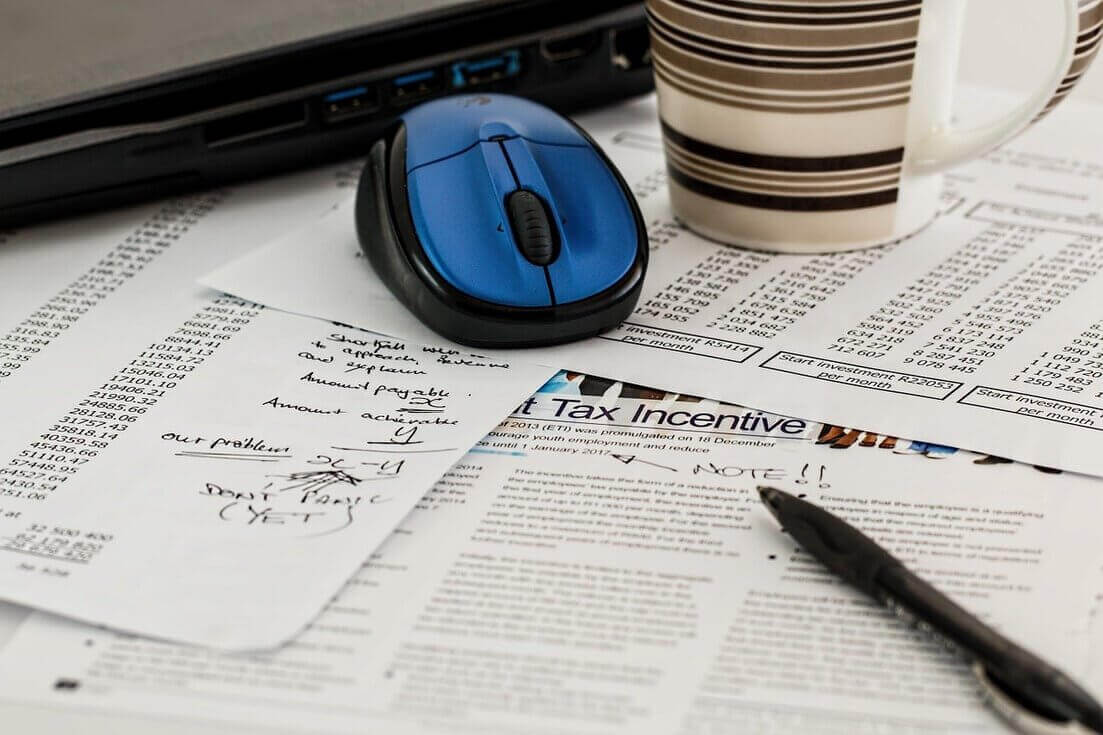 Mesa com mouse, caneca e papéis sobre escritura fiscal e tributação